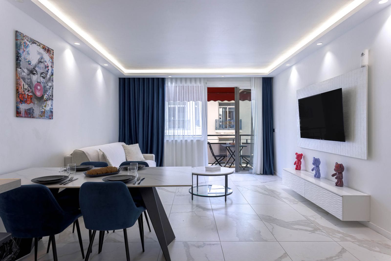 Le séjour lumineux de L'Unique Maubourg, sa table en marbre entourée de chaises en velours bleu nuit et son balcon ouvert sur Cannes.